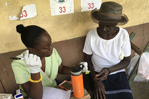 A healthcare worker is giving assistance to an older woman, handing her something that looks like a sticky note. 