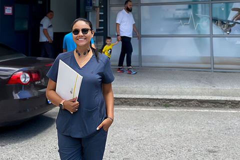  Melissa Triana recently travelled to Kosovo for an internship, where she worked with a group called Action for Mothers and Children. Photo: Courtesy of Melissa Triana By Ashley A. Williams 10-25-2022 Melissa Triana, who is studying global health and society, stands smiling in front of a building in grey scrubs. She is holding a folder. 